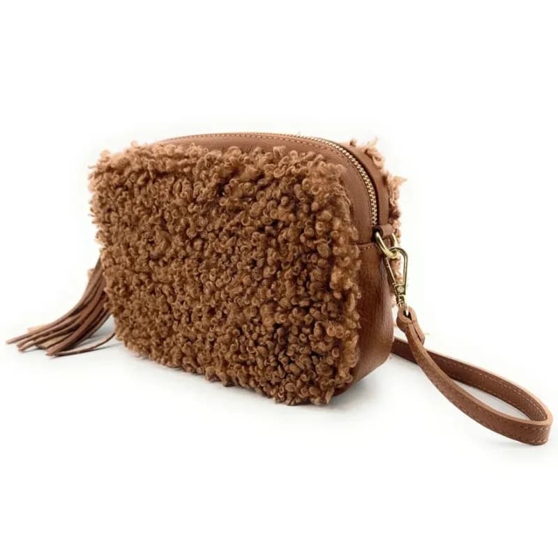 Sac rectangulaire à texture bouclette camel avec pompon, fermeture zippée dorée et dragonne assortie, vu de trois quarts sur fond blanc.