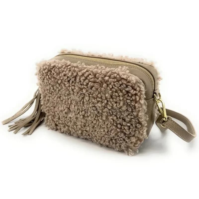 Sac rectangulaire à texture bouclette taupe rosé avec pompon, fermeture zippée dorée et dragonne assortie, vu de trois quarts sur fond blanc.